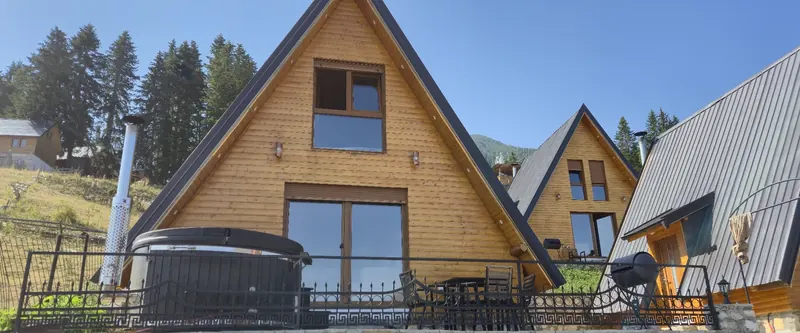 A-frame with a wooden hot tub on its fenced terrace on a sunny day