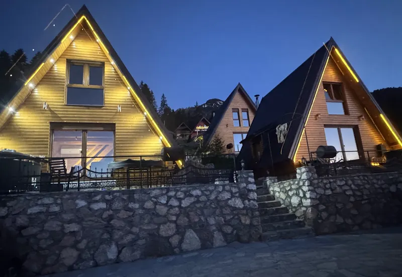 Lit A-frame villas above a stone wall in the blue hour