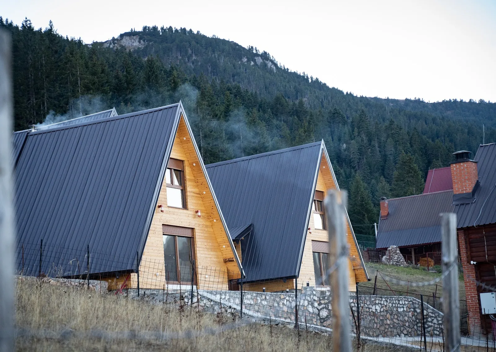 Two A-frames below a forested peak, smoke rising from the chimney