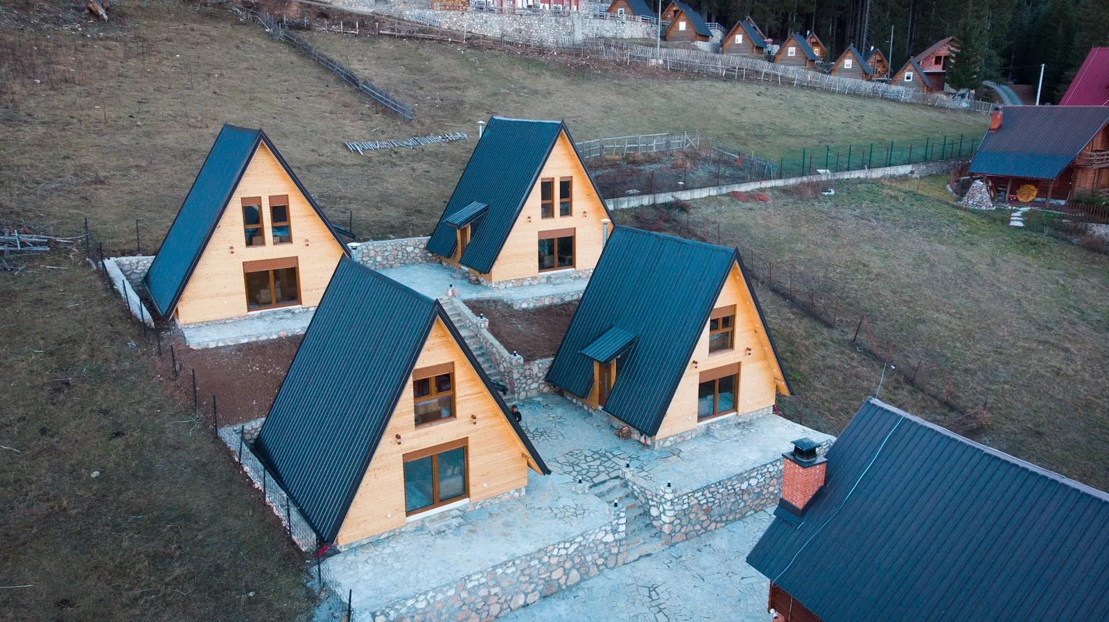 Aerial view of the four A-frame villas with stone terraces on the meadow at Liqenat