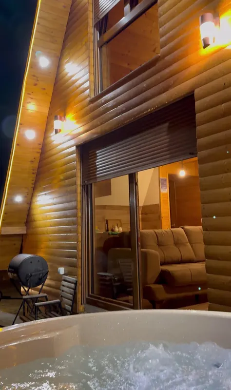 Bubbling jacuzzi on the terrace of an A-frame at night, warm lights on the wooden facade