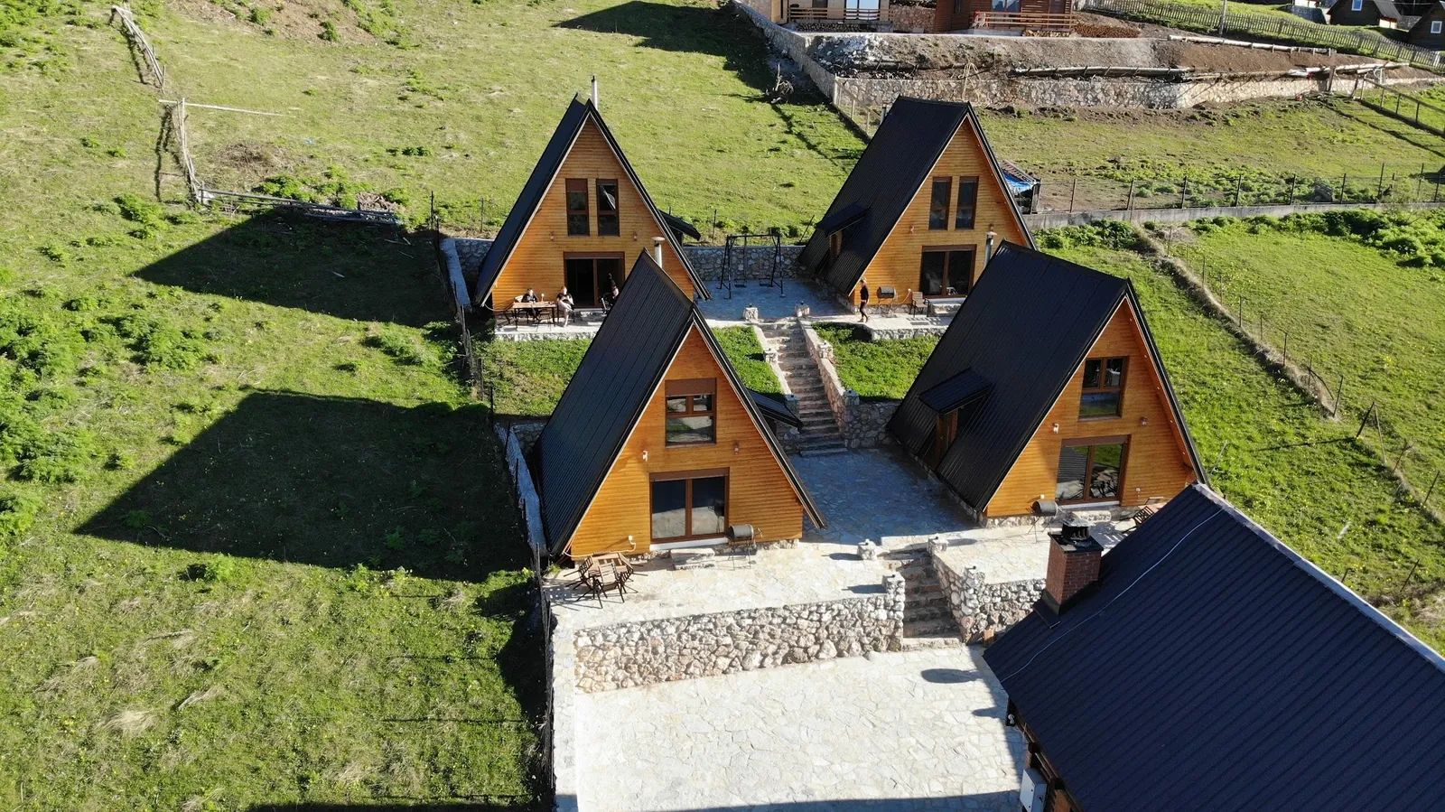Summer aerial view of the four A-frame villas and their stone terraces on a green Rugova meadow
